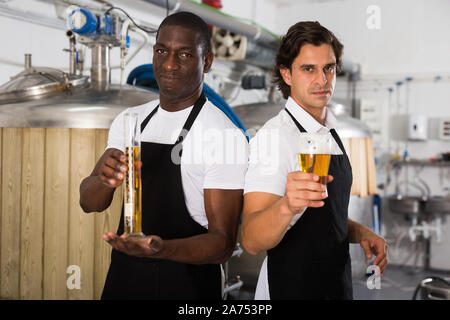 Due produttori professionali che mostra il vetro e il pallone di birra nella fabbrica di birra Foto Stock