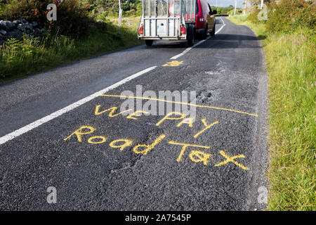 Segni di protesta verniciato a spruzzo sul manto stradale in Irlanda di lamentarsi della scarsa manutenzione delle strade. Dobbiamo pagare la tassa di circolazione Foto Stock