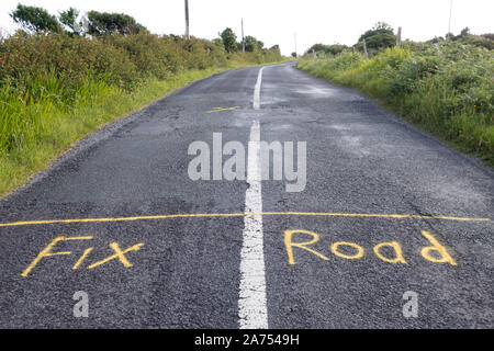 Segni di protesta verniciato a spruzzo sul manto stradale in Irlanda di lamentarsi della scarsa manutenzione delle strade. Dobbiamo pagare la tassa di circolazione Foto Stock