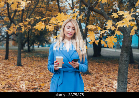 Il successo di mezza età femminile donna tramite telefono cellulare per sms o i social media in autunno park Foto Stock