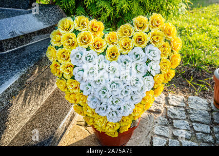 Fiori artificiali a forma di cuore si trovano accanto alla lapide nel cimitero. Foto Stock