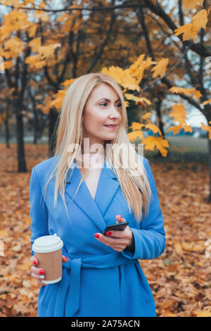 Il successo di mezza età femminile donna tramite telefono cellulare per sms o i social media in autunno park Foto Stock