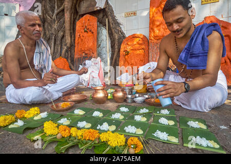 Sacerdoti indù al serbatoio Banganga in Mumbai, India preparando a condurre i riti per un defunto dalla posa delle offerte di prodotti alimentari e di calendula fiori Foto Stock