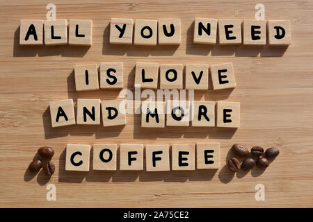 Tutto ciò di cui hai bisogno è amore e più caffè-. Parole in 3d alfabeto di legno lettere con i chicchi di caffè su un bambù Sfondo legno Foto Stock