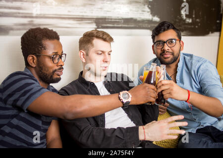 Maschio felici amici appassionati di calcio guardare partite di calcio in tv e celebrare il traguardo di bere succo di frutta e acqua frizzante seduti sul divano di casa. Amicizia, s Foto Stock