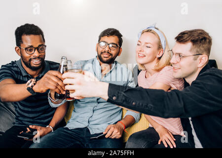 Felice multiculturale di amici studenti di indossare un abbigliamento informale a bere il tintinnio di bottiglie e bicchieri di bevande, festeggia il compleanno. Tre uomo e woma Foto Stock