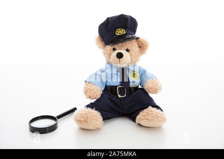 Funzionario di polizia orsacchiotto in uniforme e una lente di ingrandimento isolata contro uno sfondo bianco Foto Stock