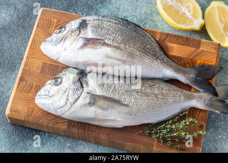 Fresh dorada con timo e limoni a metà sul pannello di legno Foto Stock