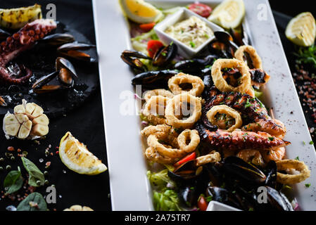 delizioso piatto di pesce fritto misto con polpo, gamberi, gamberi, conchiglie, calamari e pesce fresco - con condimento al limone e alle erbe Foto Stock