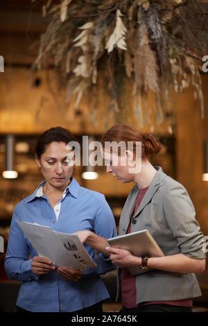 Giovane imprenditrice con tavoletta digitale rivolto alla relazione finanziaria del suo collega e discutere con lei alcuni dettagli Foto Stock