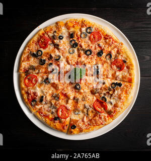 Un assortimento di pizza tagliata in pezzi al buio su un sfondo di legno Foto Stock