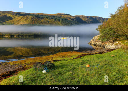 Una nebbiosa mattina colpo di una barca e bassa velatura giace sulle sponde del Loch Teacuis, Morvern, Highlands scozzesi, Scozia Foto Stock