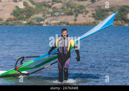 Windsurf con scheda di surf e vela in uscita dall'acqua. Foto Stock