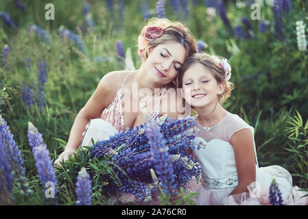 Madre e figlia la raccolta di fiori di lupino in un bellissimo campo sul tramonto. Bella ragazza in abito viola tenendo un lupino al tramonto sul campo. Il Foto Stock