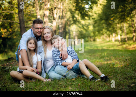 La famiglia felice di quattro seduti su un prato in estate parco all'aperto e sorridente Foto Stock