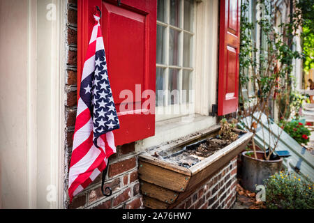 Una bandiera americana pende da una serranda su una vecchia casa di Philadelphia. Foto Stock