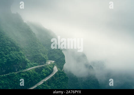 Coperto da nuvole basse e la nebbia pericoloso sterzate brusche sulla strada di avvolgimento di 99 spire alla sommità della montagna Tianmen, Zhangjiajie National Park, Hu Foto Stock