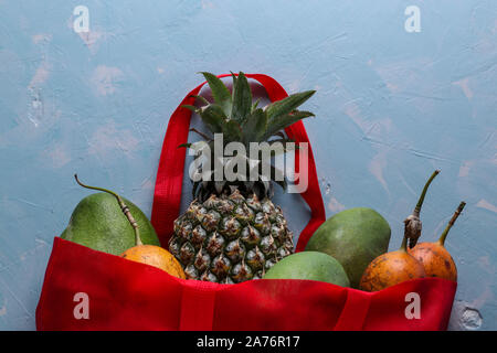 Rifiuti Zero concetto, rosso tessile shopping bag con fresca frutta tropicale: mango, ananas e frutto della passione su fondo azzurro Foto Stock