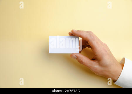 Maschio lato tenendo un blank business card su morbido sfondo giallo per il testo o per il design. Blank carta di credito i modelli per contatto o utilizzare in azienda. Finanza, ufficio. Mock up. Copyspace. Foto Stock