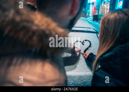 Giovane adulto giovane disegna un cuore sulla neve auto coperto Foto Stock