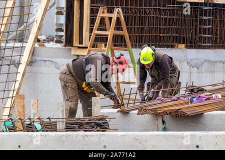 Lavoratori edili piegatura - cablaggio calcestruzzo barre di acciaio all'aperto in Nuuk. Foto Stock