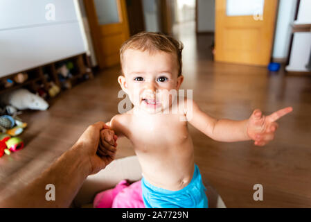 Bella e adorabile uno-anno-vecchia ragazza ad imparare a camminare sorrisi mentre suo padre trattiene la sua mano. Foto Stock