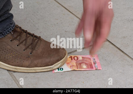 Qualcuno ha trovato 10 euro sulla strada, fissandolo con il suo piede, il tentativo di afferrare la banconota. La mano è fuori fuoco per il movimento e la dinamica. Foto Stock