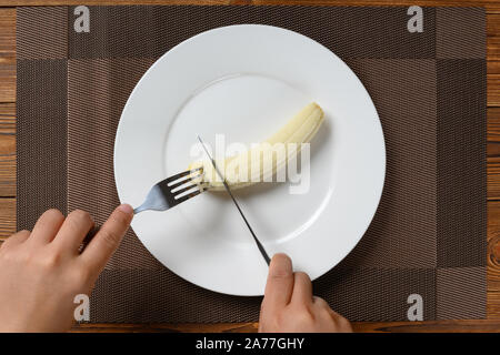 Vista dall'alto uomo mangiare una banana fresche con la forchetta e coltello Foto Stock
