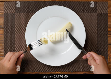 Vista dall'alto uomo mangiare una banana fresche con la forchetta e coltello Foto Stock