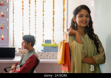 Giovane donna in piedi in ufficio tenendo le borse della spesa in mano durante il Diwali celebrazioni. Foto Stock