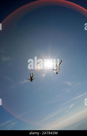 Questi due skydivers sono volare alto nel cielo blu intorno a ogni altro e la riproduzione di dischi per catturare le mani. Ogni subacqueo ha divertimento e un grande sorriso sul suo volto. Foto Stock