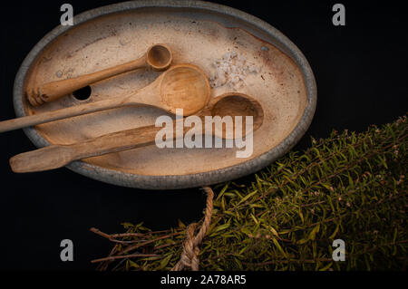 Tre cucchiai di legno su un vaso di ceramica con un fascio di erbe salato.su uno sfondo nero. vista dall'alto. Foto Stock