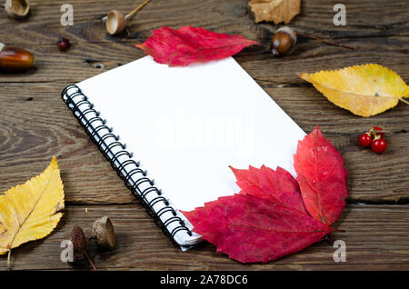 In autunno la composizione su sfondo di legno . Blank notepad coperto con autunno foglie di ruggine, castagne, ghiande, rowan bacche . Vista dall'alto , lo spazio di copia . Foto Stock