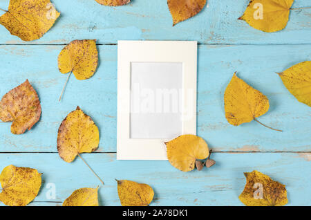 Composizione di autunno sfondo. Rusty foglie di giallo su sfondo blu bordo con un vuoto di photo frame nel centro .vista superiore, copia dello spazio, laici piana . Foto Stock