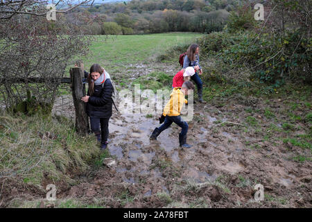 Bambini in famiglia che camminano attraverso una puzza di fango immersi nel fango di campagna durante una pausa di mezza pensione in autunno nel Carmarthenshire Galles Regno Unito KATHY DEWITT Foto Stock