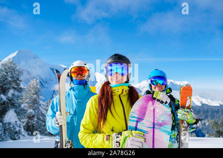 Uomo e donna con lo snowboard e sci permanente sulla neve località contro il fondale di montagna nel pomeriggio. Foto Stock