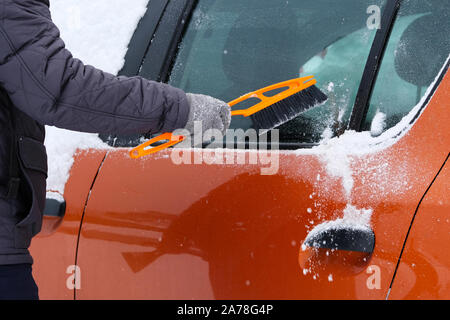 Auto coperti di neve. L'uomo la spazzolatura e spalare la neve auto off dopo la tempesta di neve. Spazzola in mano mans. Foto Stock