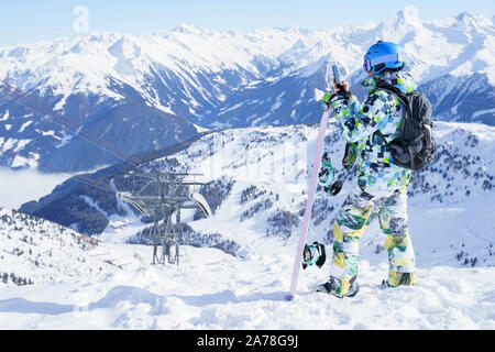 Foto dal retro dello sport uomo nel casco, con lo snowboard e in phone in mani alla stazione sciistica Foto Stock