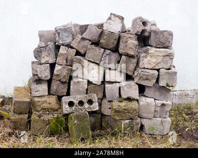 Una pila di vecchi mattoni grigio su un muro di cemento sullo sfondo Foto Stock