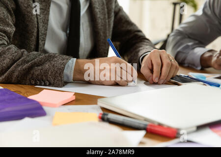 I giovani professionisti di aziende aventi una riunione. Diversi gruppi di colleghi discutere nuove decisioni, dei piani per il futuro e la strategia. Ambiente di lavoro creativo, finanza, il lavoro di squadra. Close up di mani e oggetti personali. Foto Stock