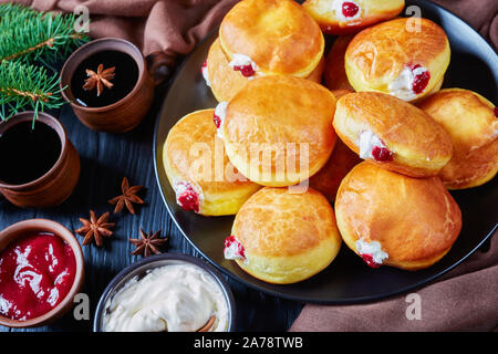 Close-up di Berliner Pfannkuchen, Tedesco Ciambelle con marmellata di lamponi e ripieni di crema su una piastra. arti fir e tazze di caffè nero a tavola in legno Foto Stock