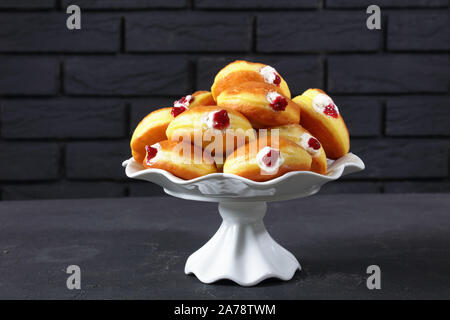 Berliner Pfannkuchen, Tedesco Ciambelle con marmellata di lamponi e ripieni di crema su una torta a stare su un tavolo di cemento con un muro di mattoni in background Foto Stock
