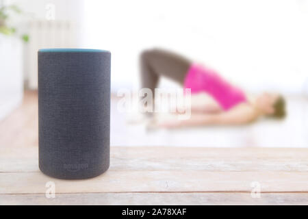 Alexa echo plus dispositivo con una specialità per il fitness e una ragazza facendo alcuni hip raisesworkout a casa. Svuotare lo spazio di copia per l'editor di testo Foto Stock