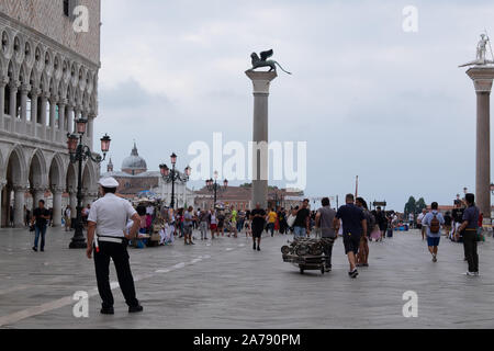 Poliziotto locale a guardare i tanti turisti e le consegne di Piazza San Marco a Venezia con i famosi pilastri su visualizza Foto Stock