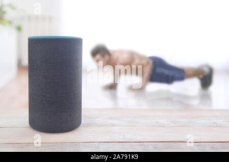 Alexa echo plus dispositivo con una specialità di fitness e un uomo facendo qualche spinta in su allenamento a casa. Svuotare lo spazio di copia per l'editor di testo Foto Stock