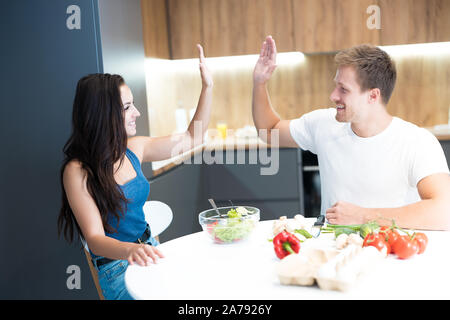 Coppia giovane bello il marito e la sua bella moglie cucinare la colazione nella cucina insieme dando alta cinque cercando felice il lavoro di squadra Foto Stock