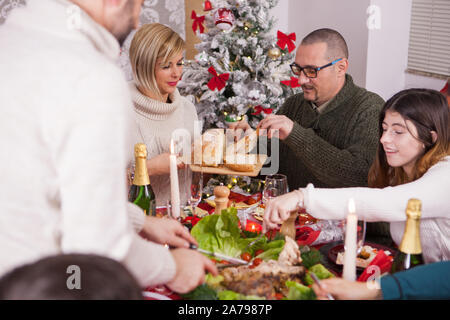 Donna passando il pane sulla tavola per suo marito a festa di natale. Cibo tradizionale per il natale. Famiglia festeggiano il Natale insieme. La felicità intorno al tavolo in festa di natale. Foto Stock