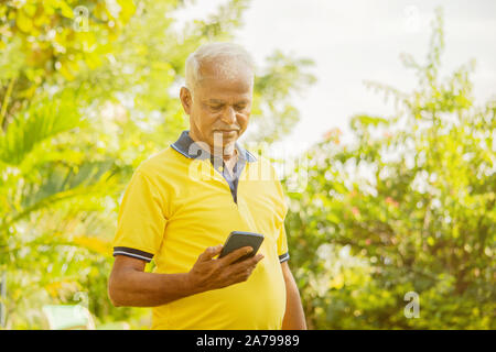 Senior uomo cercando il telefono - vecchia persona maschio utilizzando mobile presso il park - cittadini anziani sullo smartphone all'aperto. Foto Stock