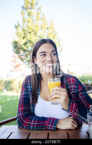 Ritratto di giovane sorridenti donna bere il succo d'arancia per esterno Foto Stock