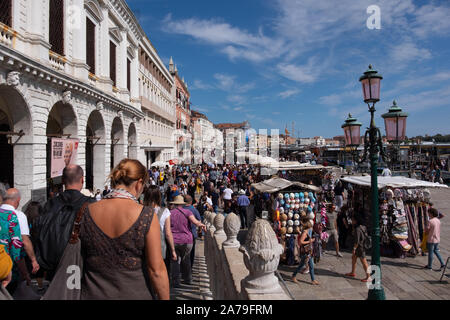 Enormi folle di turisti sul lato del canale da Piazza San Marco, Venezia. Guardando verso il basso i passi verso i molti mobili di bancarelle turistiche del negozio di souvenir Foto Stock